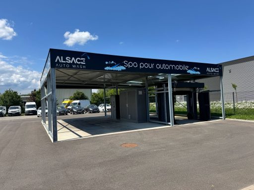 Abri de stationnement couvert avec publicité, ciel bleu et véhicules en arrière-plan.